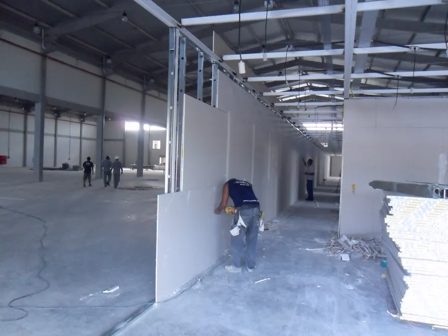Instalador montando paredes de drywall em galpão comercial